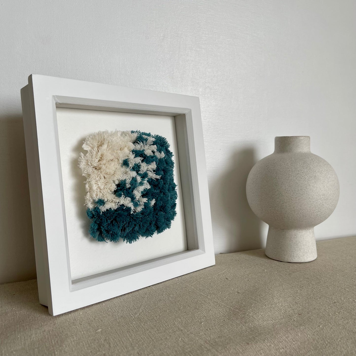 Ocean teal and cream fluffy textured woven wall art in a square white painted wood deep box frame next to scandi vase