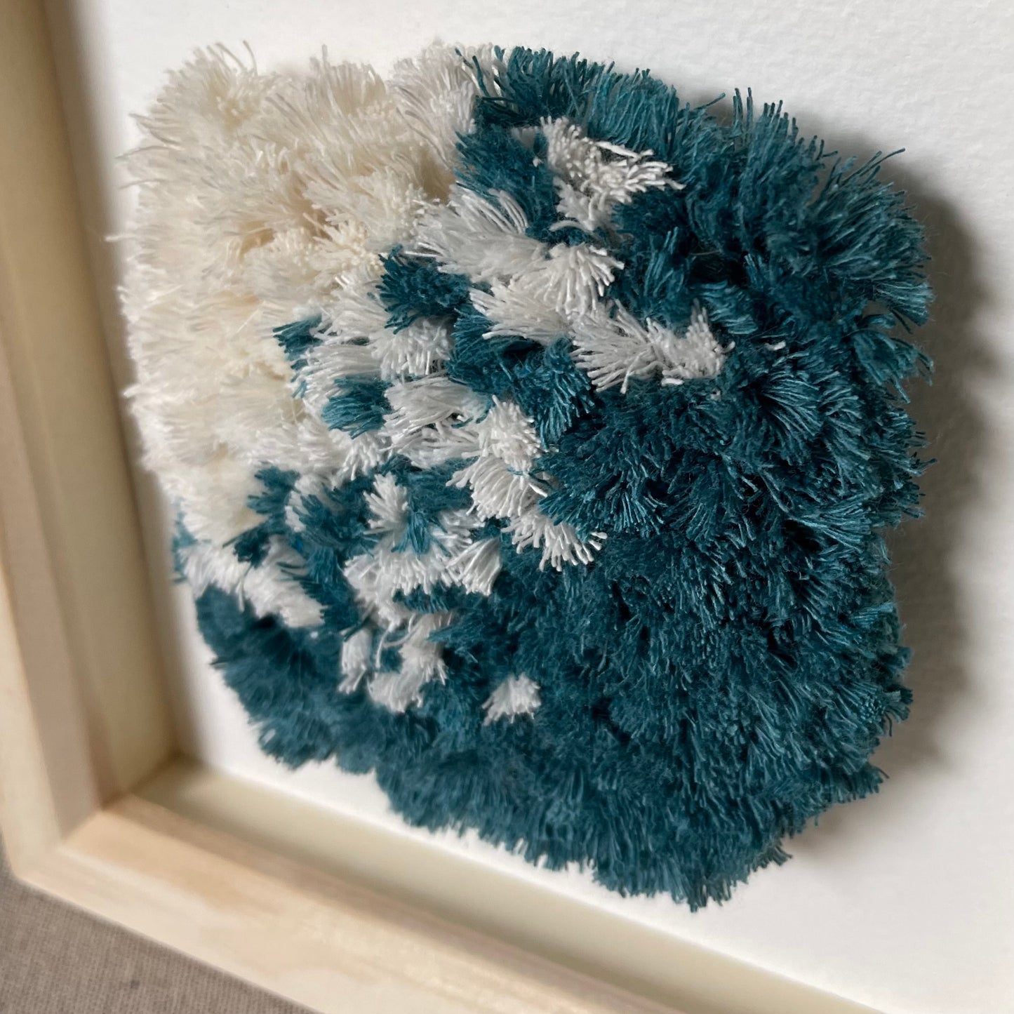 Close up view of ocean teal and cream fluffy textured woven wall art in a square wood deep box frame