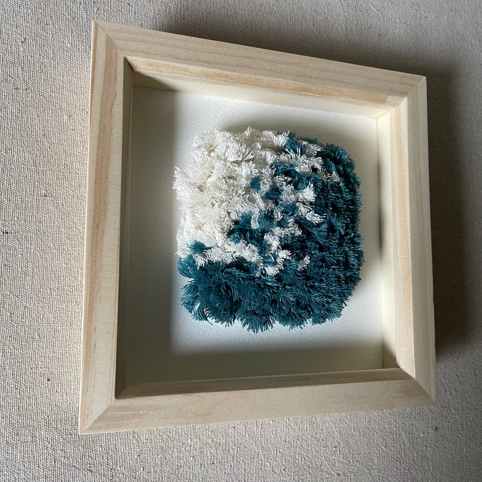 Ocean teal and cream fluffy textured woven wall art in a square wood deep box frame in sunlight