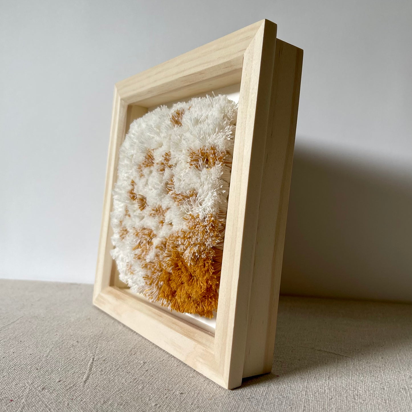 Side view of cream and yellow ochre fluffy textured woven textile art in natural wood deep box frame