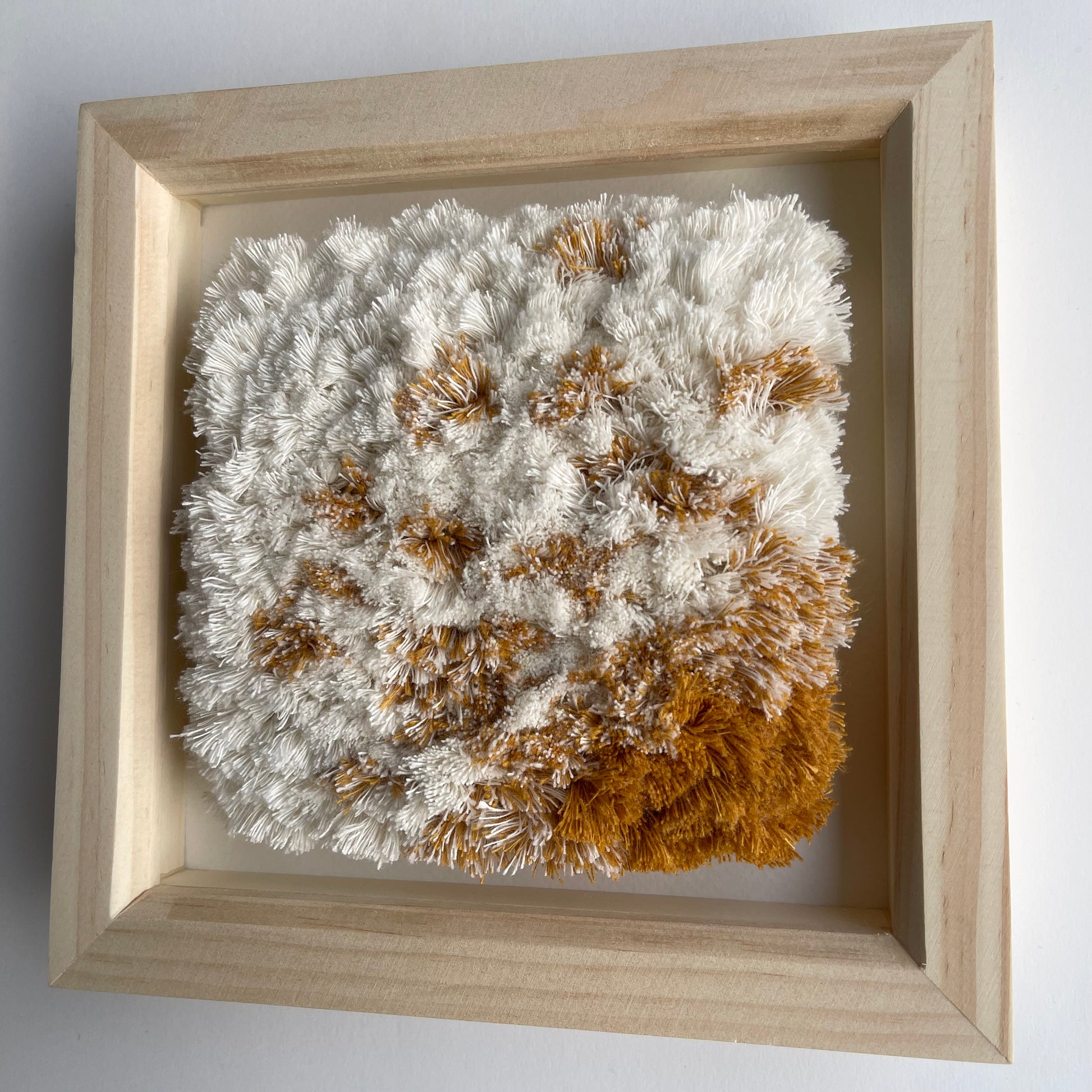 Cream and yellow ochre fluffy textured woven textile art in natural wood deep box frame on wall
