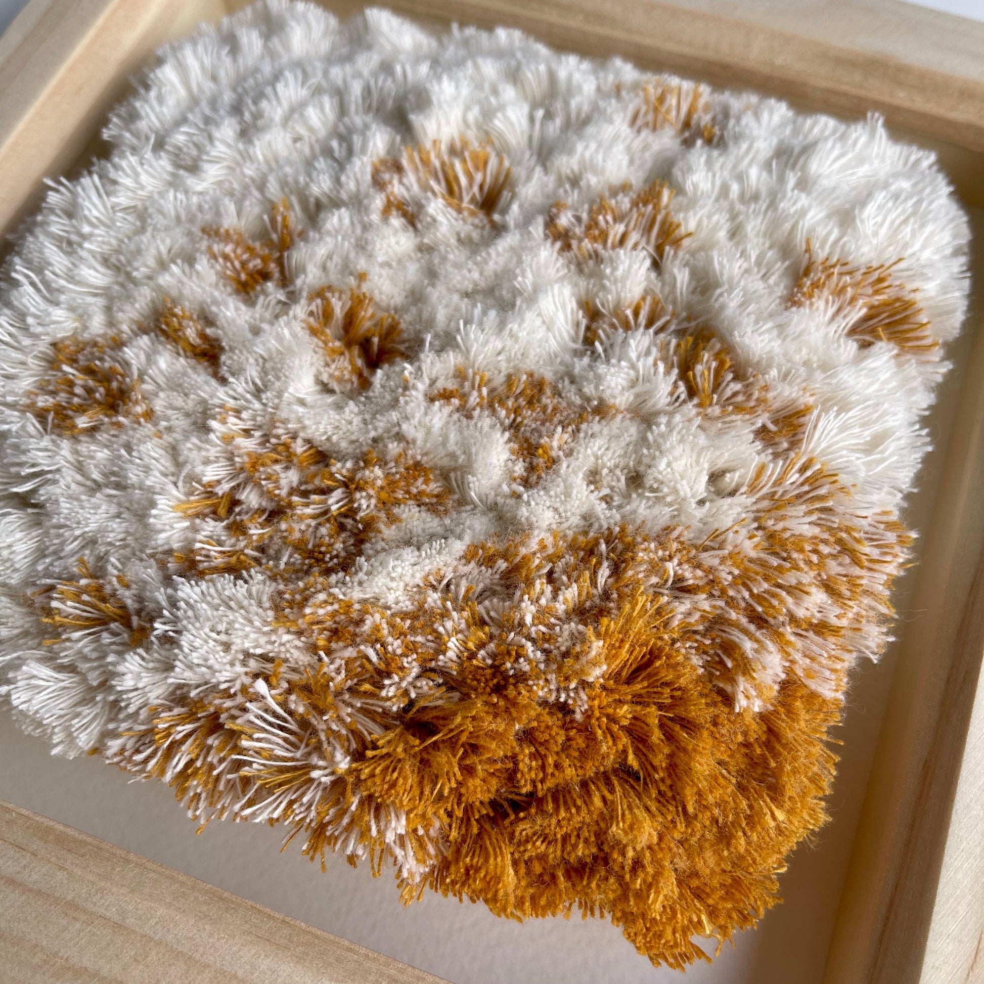 Close up detail of yellow ochre and cream fluffy woven textile art in natural wood frame